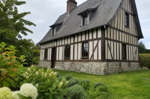 Maison normande traditionnelle avec colombages, soubassement en pierre et toiture pentue