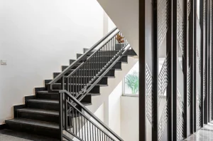 Escalier intérieur à marches sombres avec garde-corps métallique dans une cage d’escalier claire